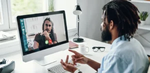 Busy man in shirt talking with his coworker using computer while sitting indoors